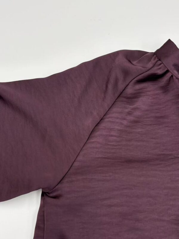Close-up of a luxurious burgundy satin blouse with a high collar and subtle sheen, perfect for formal or evening wear.