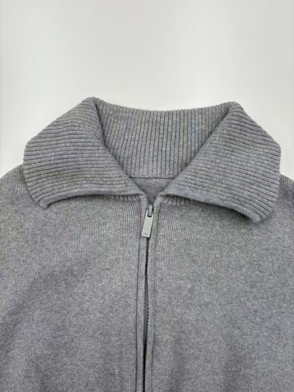 Close-up of a gray zip-up sweater with a ribbed collar, suitable for casual or athletic wear, made from comfortable knit fabric.