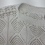 Close-up of a stylish, cream-colored knitted sweater with intricate lace and cable patterns, perfect for fall and winter fashion.
