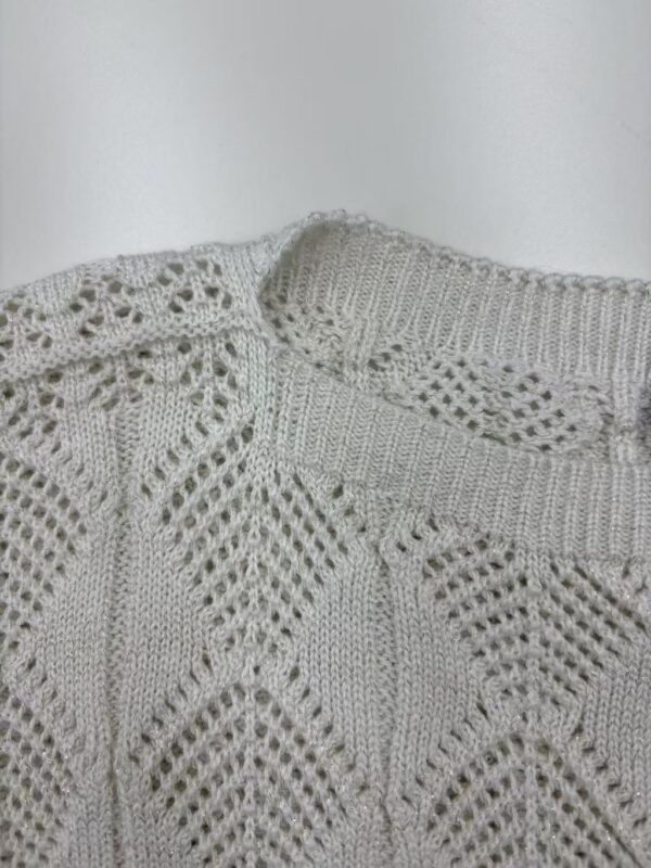 Close-up of a stylish, cream-colored knitted sweater with intricate lace and cable patterns, perfect for fall and winter fashion.