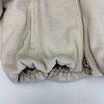 Close-up of a cream-colored fleece jacket featuring a zipper and side pocket, showcasing soft fabric and casual style.