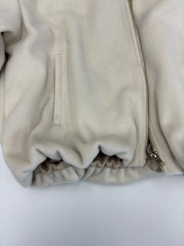 Close-up of a cream-colored fleece jacket featuring a zipper and side pocket, showcasing soft fabric and casual style.