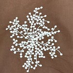 Close-up of intricate white beaded embroidery on brown fabric, showcasing detailed craftsmanship and delicate beadwork.