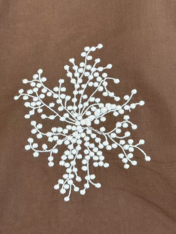 Close-up of intricate white beaded embroidery on brown fabric, showcasing detailed craftsmanship and delicate beadwork.