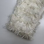Close-up of a cream-colored textured fabric with intricate woven patterns and fringed edges, ideal for fashion or home decor.