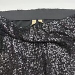 Close-up of a black sequin dress showing shiny, reflective sequins and a hint of the neckline, perfect for evening wear or special occasions.