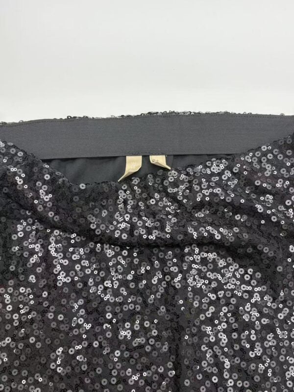 Close-up of a black sequin dress showing shiny, reflective sequins and a hint of the neckline, perfect for evening wear or special occasions.