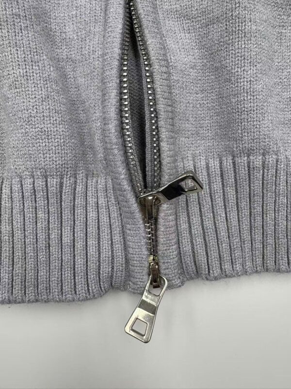 Detailed view of a grey hoodie with a silver zipper and ribbed hem, showcasing casual fashion and comfortable fabric.