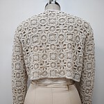 Close-up of a beige crochet knit sweater displayed on a mannequin, showcasing intricate floral and geometric patterns for a stylish look.