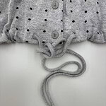 Close-up of a gray polka dot sweater with buttons and a drawstring at the hem, showcasing casual fashion style.
