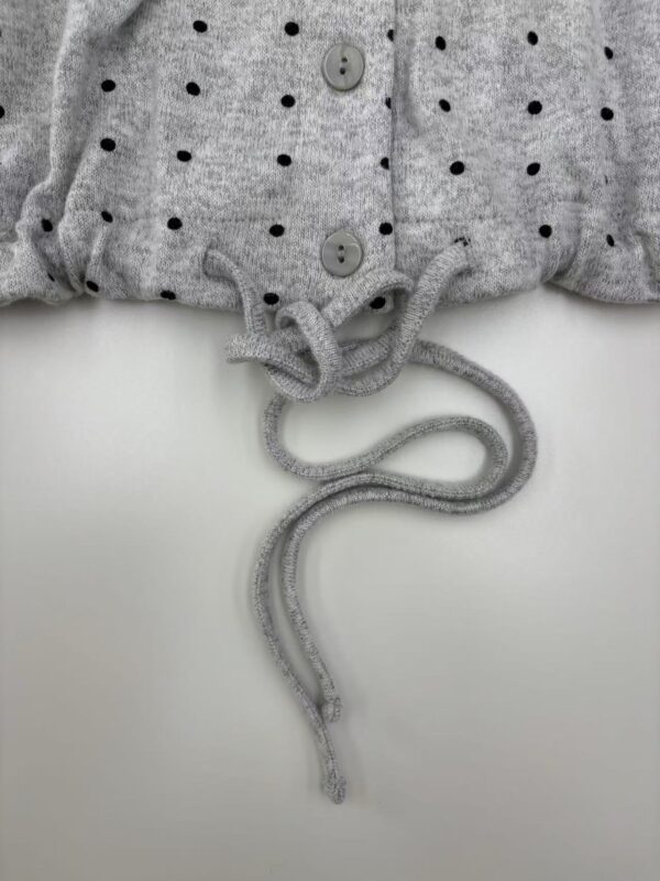 Close-up of a gray polka dot sweater with buttons and a drawstring at the hem, showcasing casual fashion style.