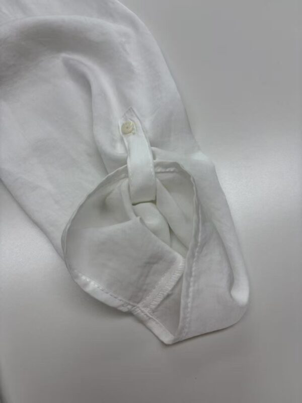 Close-up of a white dress shirt sleeve with a buttoned cuff, showcasing fine fabric and stitching for formal wear.