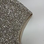 Close-up of silver sequin fabric with a beige trim, ideal for glamorous clothing and accessories.