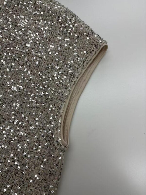 Close-up of silver sequin fabric with a beige trim, ideal for glamorous clothing and accessories.