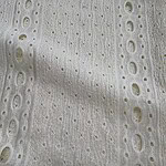 Close-up of white eyelet fabric with intricate cut-out patterns, ideal for stylish clothing and accessories.