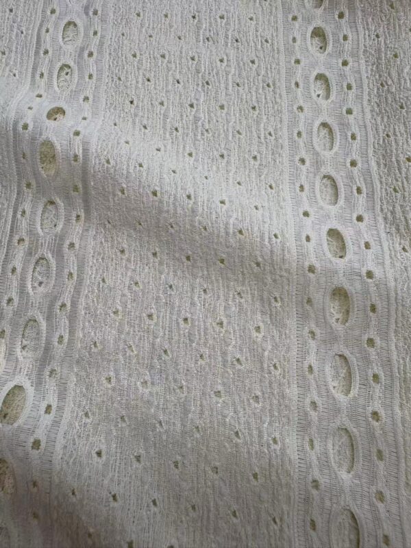 Close-up of white eyelet fabric with intricate cut-out patterns, ideal for stylish clothing and accessories.