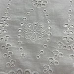 Close-up of white fabric with intricate embroidery featuring floral and geometric patterns, showcasing fine craftsmanship and delicate detailing.