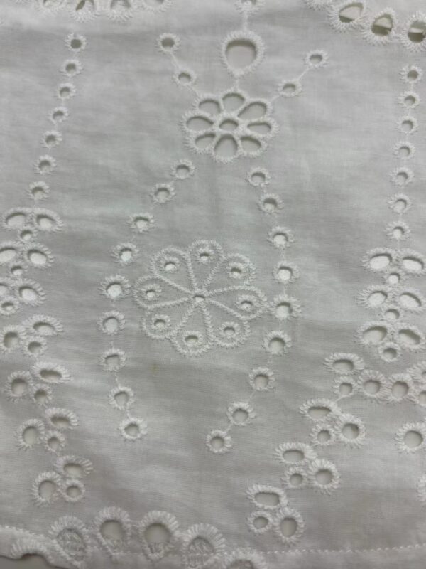 Close-up of white fabric with intricate embroidery featuring floral and geometric patterns, showcasing fine craftsmanship and delicate detailing.