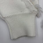 Close-up of a cream-colored knit sweater sleeve with ribbed cuff and frayed edge detail, showcasing soft fabric and craftsmanship.