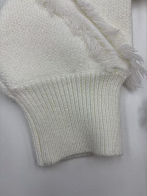 Close-up of a cream-colored knit sweater sleeve with ribbed cuff and frayed edge detail, showcasing soft fabric and craftsmanship.
