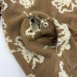 Close-up of a brown wool coat with intricate white embroidery and metallic buttons, showcasing high-quality craftsmanship and stylish design.