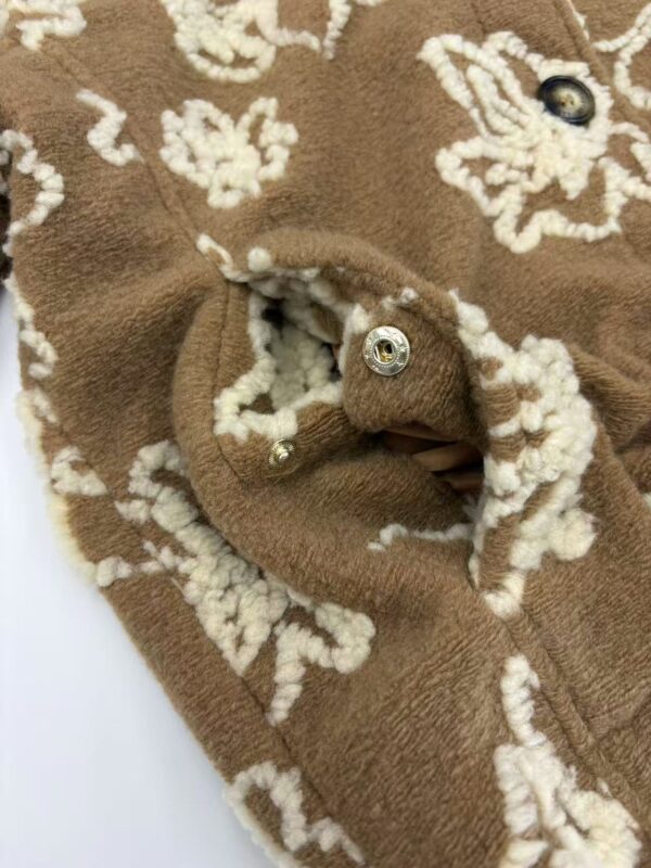 Close-up of a brown wool coat with intricate white embroidery and metallic buttons, showcasing high-quality craftsmanship and stylish design.