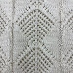 Close-up of a cream-colored knitted sweater with intricate diamond and lattice patterns, showcasing fine craftsmanship and texture.