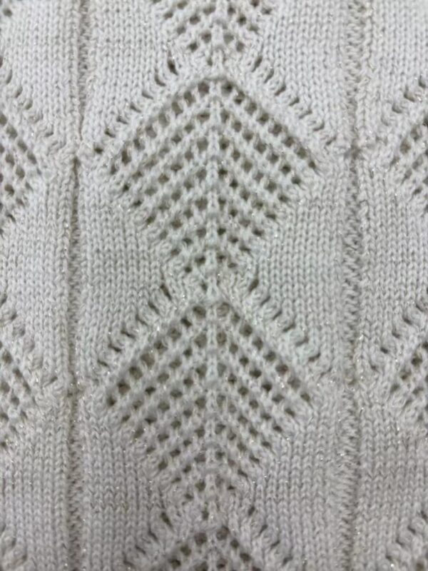 Close-up of a cream-colored knitted sweater with intricate diamond and lattice patterns, showcasing fine craftsmanship and texture.