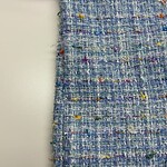 Close-up of vibrant tweed fabric with multicolored threads, showcasing texture and intricate weaving suitable for high-end fashion garments.