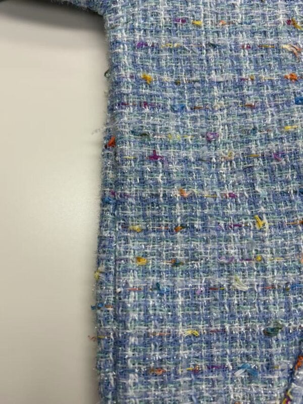 Close-up of vibrant tweed fabric with multicolored threads, showcasing texture and intricate weaving suitable for high-end fashion garments.