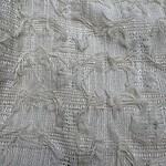 Close-up of intricate white lace fabric with textured patterns and delicate details, ideal for fashion and dressmaking.