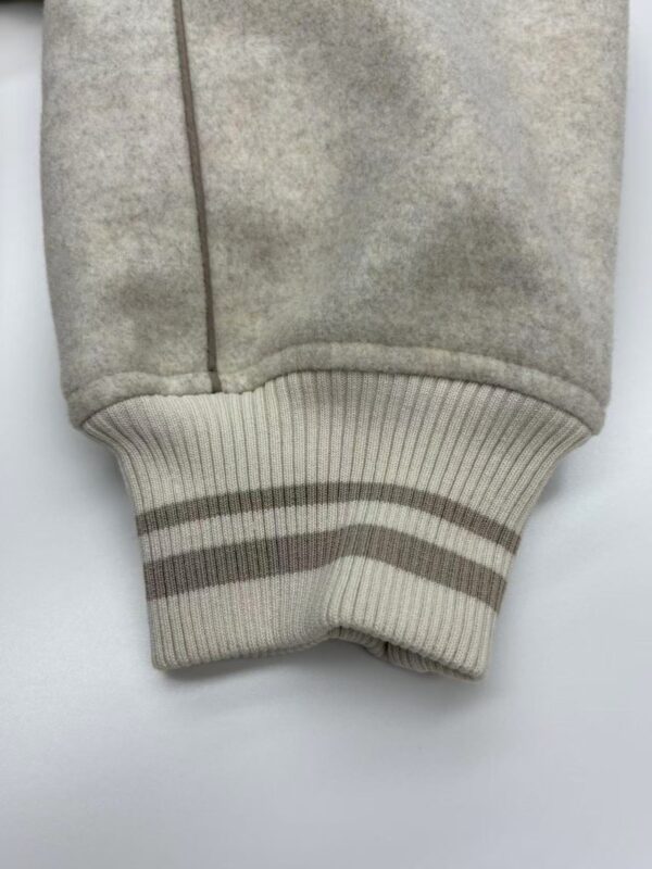 Close-up of beige sweatshirt cuff featuring ribbed knit and two horizontal stripes, showcasing casual fashion style.