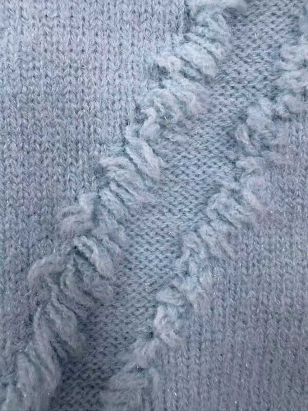 Close-up of light gray knitted fabric with textured pattern and frayed edges, showcasing soft and cozy material suitable for sweaters or scarves.
