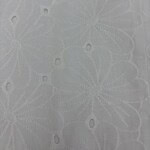 Close-up of white fabric with intricate embroidered floral patterns and eyelet details, ideal for fashion and dressmaking.