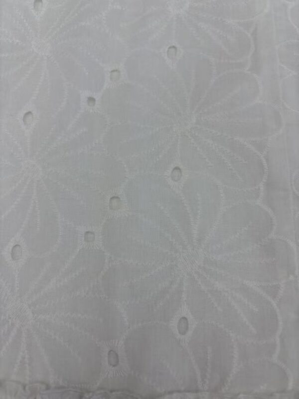 Close-up of white fabric with intricate embroidered floral patterns and eyelet details, ideal for fashion and dressmaking.