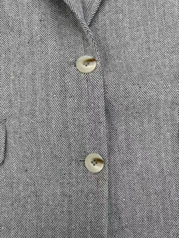 Close-up of a tailored suit fabric with a classic herringbone pattern and two cream-colored buttons.
