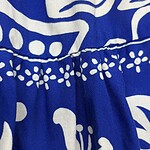 Close-up of vibrant blue fabric with white floral and abstract patterns, showcasing detailed stitching and a gathered section for a stylish garment.