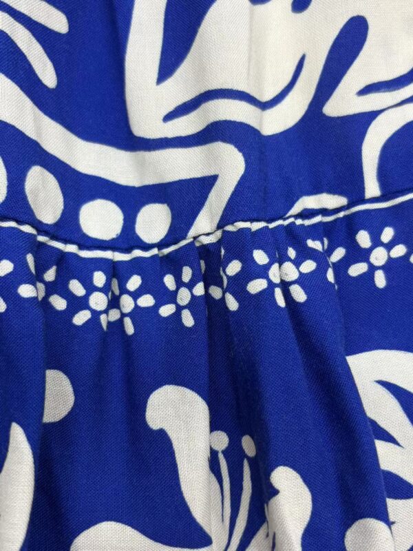 Close-up of vibrant blue fabric with white floral and abstract patterns, showcasing detailed stitching and a gathered section for a stylish garment.