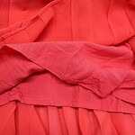 Close-up of vibrant red fabric with detailed stitching and pleats, showcasing high-quality textile craftsmanship for fashion apparel.