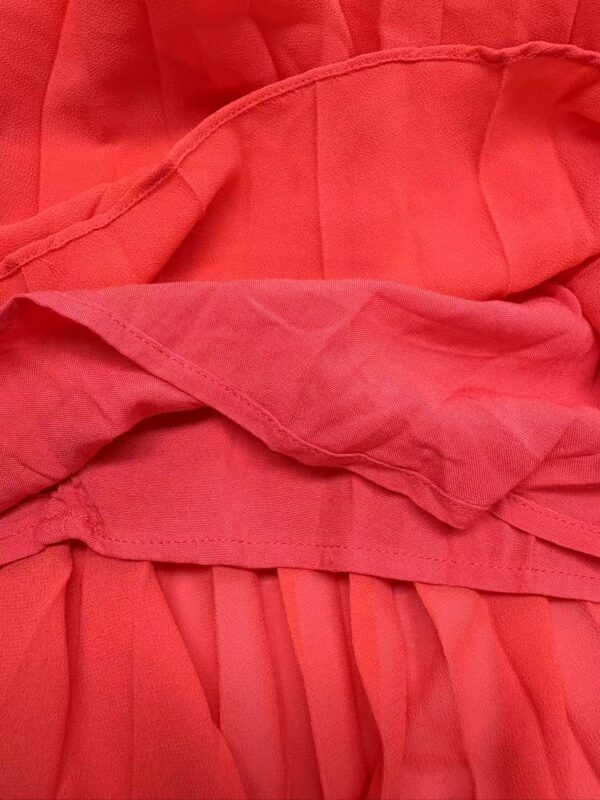 Close-up of vibrant red fabric with detailed stitching and pleats, showcasing high-quality textile craftsmanship for fashion apparel.