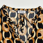 Close-up of a fashionable women's blouse with geometric circle pattern in black, beige, and orange, featuring a tie-neck detail and ruffled collar.