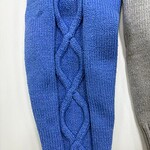Close-up of a blue cable knit sweater sleeve with intricate braided pattern, showcasing high-quality wool material and craftsmanship.