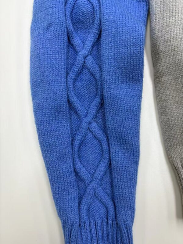 Close-up of a blue cable knit sweater sleeve with intricate braided pattern, showcasing high-quality wool material and craftsmanship.