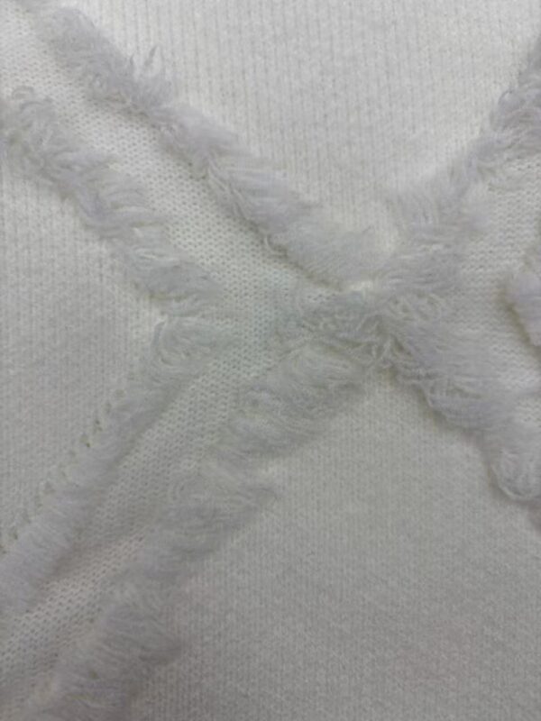 Close-up of white fabric featuring textured surface and frayed edges, ideal for fashion or textile design.