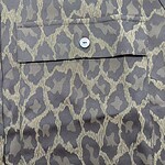 Close-up of leopard print fabric featuring a small button and pocket detail, showcasing stylish and trendy textile design for fashion apparel.