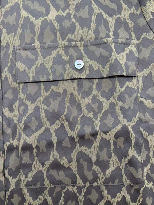 Close-up of leopard print fabric featuring a small button and pocket detail, showcasing stylish and trendy textile design for fashion apparel.