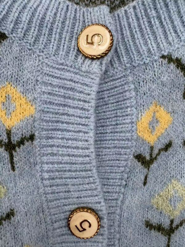 Close-up of a light blue knitted cardigan featuring yellow and black geometric patterns and gold buttons with the number 5.