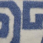 Detailed close-up of embroidered fabric showing blue thread on white background, highlighting texture and stitching.