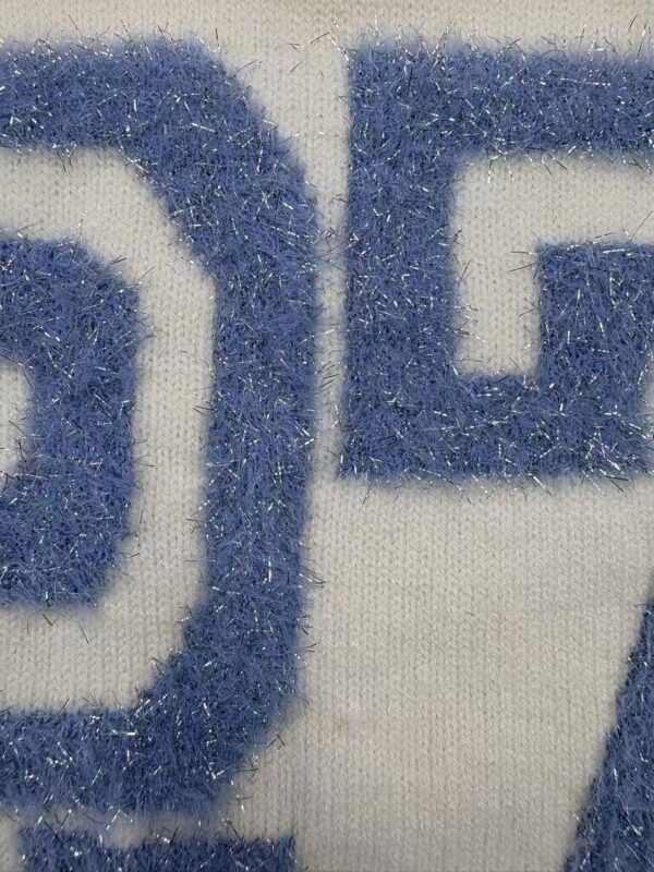 Detailed close-up of embroidered fabric showing blue thread on white background, highlighting texture and stitching.