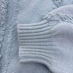 Close-up of a light blue knit sweater showing detailed stitching and ribbed cuff, highlighting cozy fabric and craftsmanship.